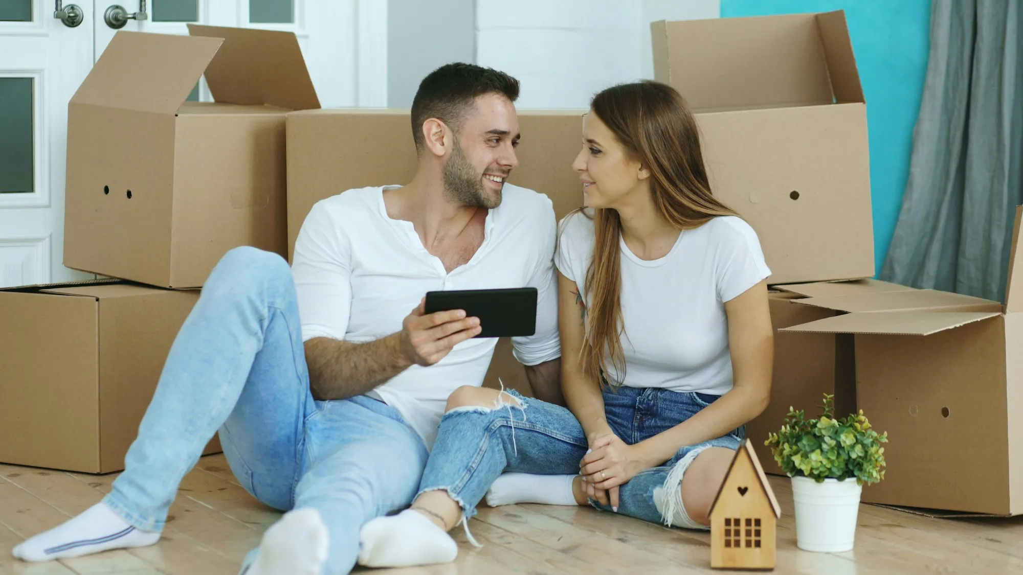 Couple sitting on the floor with a tablet surrounded by moving boxes